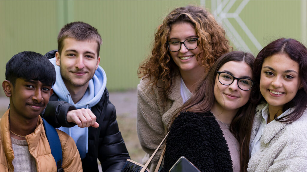 Eine Gruppe von glücklichen Jugendlichen steht vor einer grünen Wand.