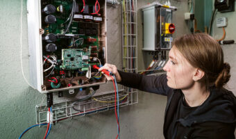 Eine Frau prüft mit einem Multimeter den Stromfluss in einem Stromkasten.