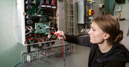 Eine Frau prüft mit einem Multimeter den Stromfluss in einem Stromkasten.