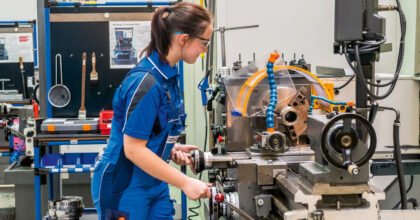 Eine Frau bearbeitet an einer Maschine ein Metallteil.